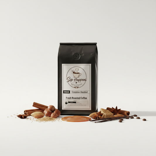 A black bag of Sip Happens Coffee, Cinnamon Hazelnut, standing upright on a light gray studio background with coffee-roasting ingredients like cinnamon sticks, star anise, whole beans, and ground coffee arranged around the base.