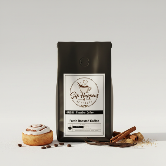 Black bag of Sip Happens Coffee, Cinnamon Bun flavor, standing on a light gray background with a cinnamon roll, cinnamon sticks, and coffee beans styled around it.